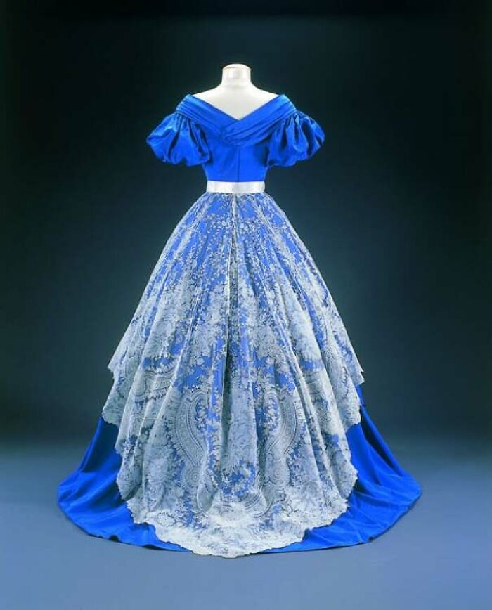 Victorian era blue and white gown with puffed sleeves and intricate lace overlay, showcasing a few centuries of fashion.