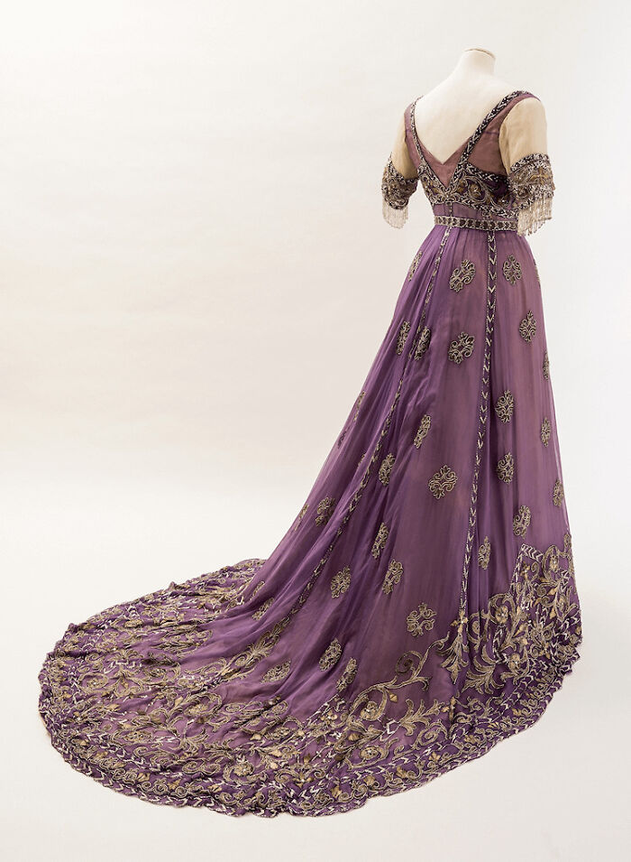 Vintage purple gown with gold embroidery and long train displayed on a mannequin, showcasing centuries of fashion history.