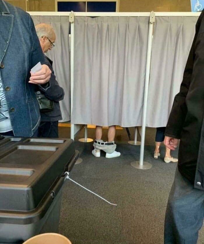 Voting booth scene showing a person with pants down and shoes on, a blursed image that may confuse the brain.