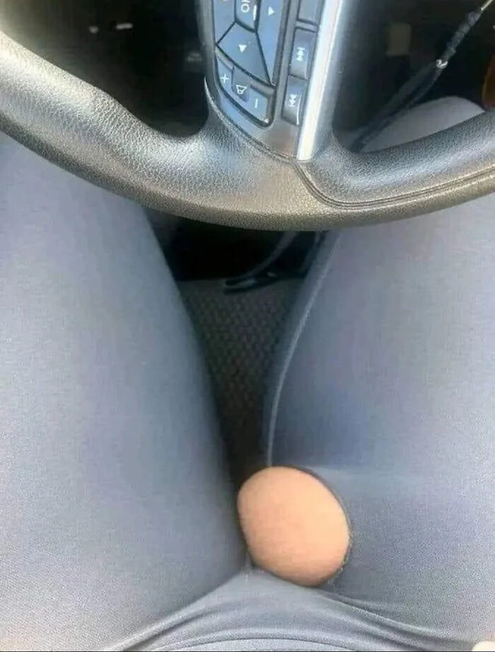 Close-up of a steering wheel and legs wearing leggings with a suspiciously placed hole revealing skin in a blursed image.