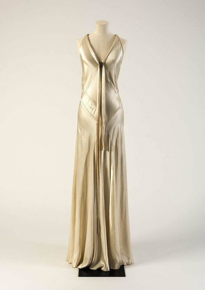 Vintage long satin evening gown in gold displayed on mannequin, showcasing centuries of fashion evolution.