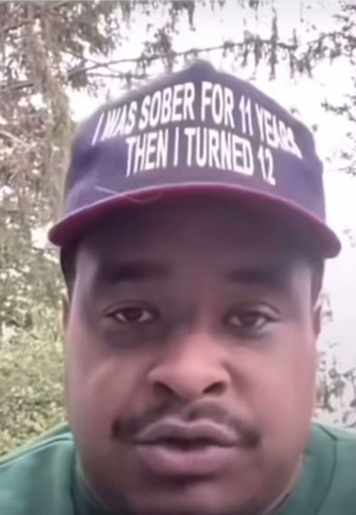 Man wearing a cap with a humorous message outdoors, an example of blursed images that may make your brain short-circuit.