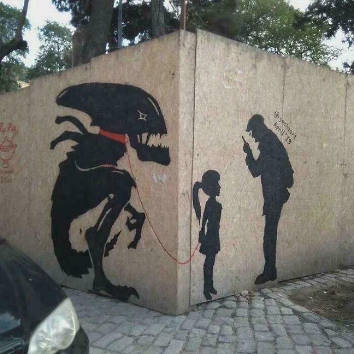 Street art showing a girl holding a leash tied to a blursed alien creature, with a man focused on his phone nearby.
