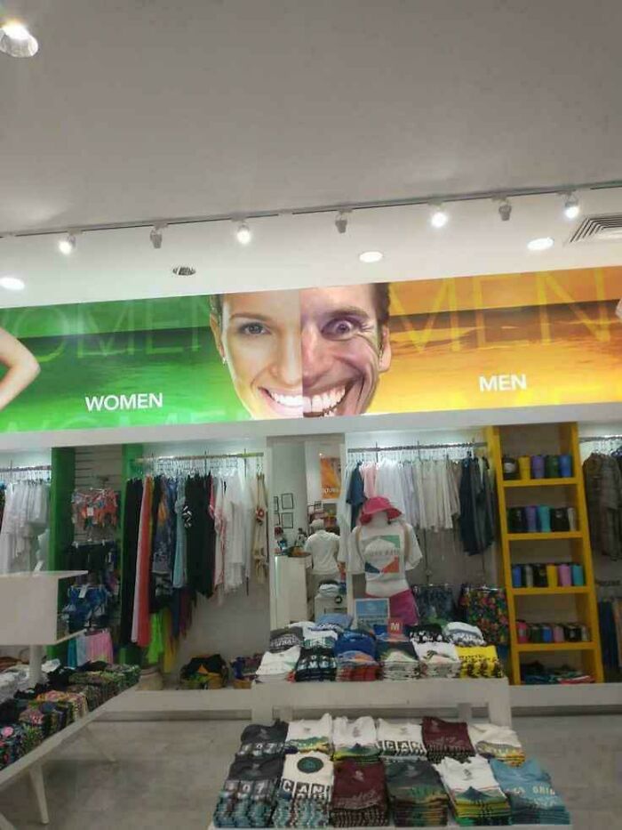 Clothing store aisle with a blursed men and women sign featuring a split face that may make your brain short-circuit.