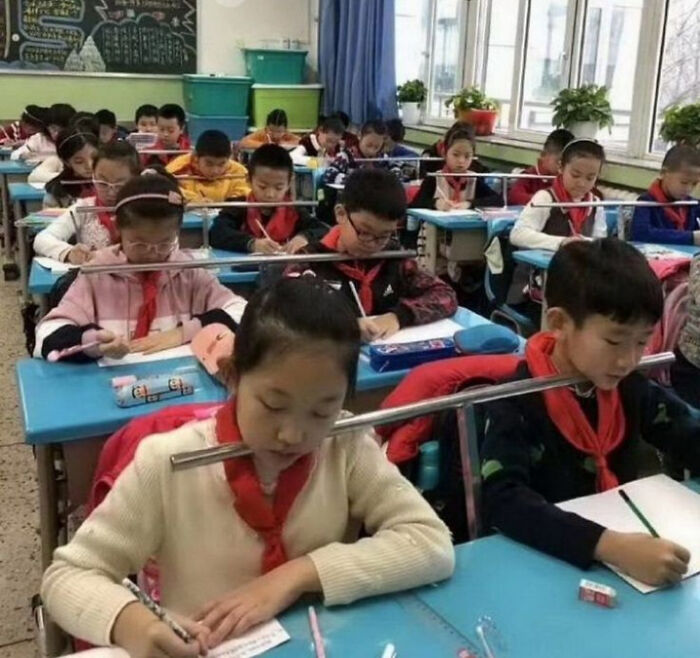 Students in a classroom with metal bars positioned unusually between their heads, a blursed image that may confuse the brain.