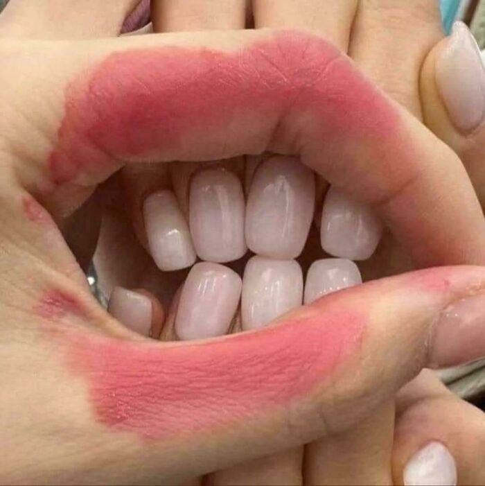 Hands with red lipstick marks positioned to form a mouth shape with nails resembling teeth in a blursed optical illusion.