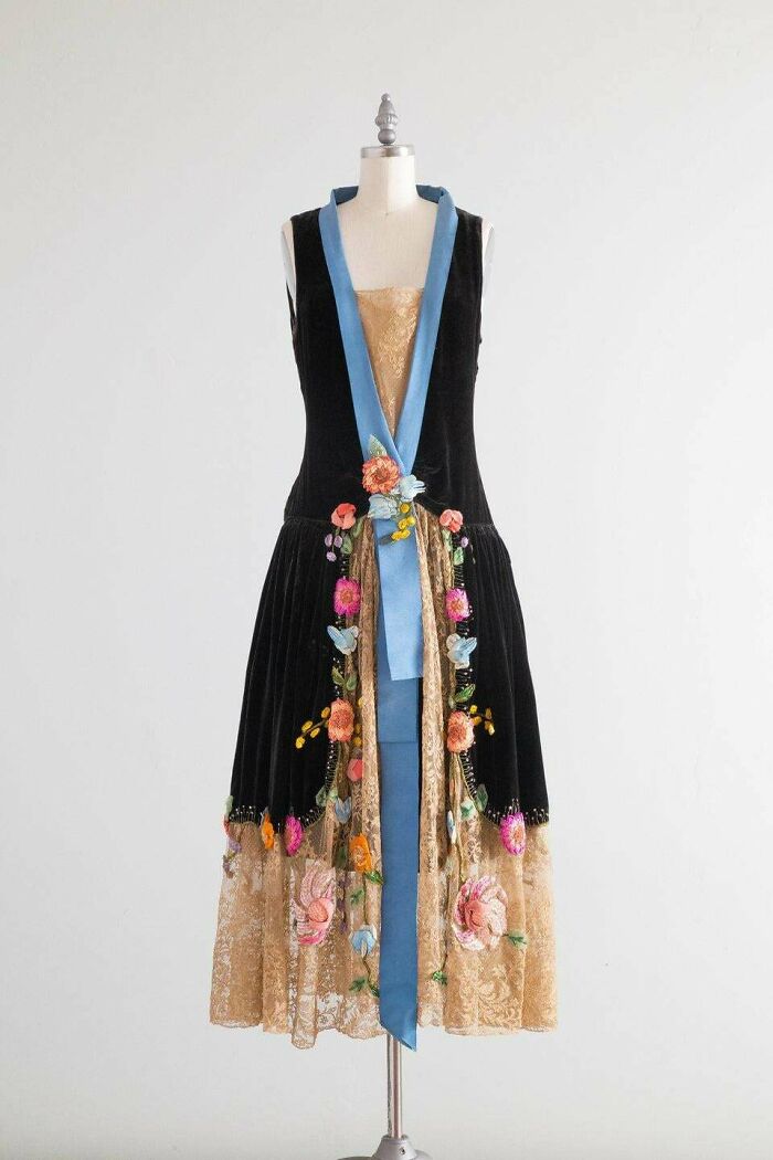 Vintage black dress with blue accents and floral embroidery, showcasing centuries of fashion history on a mannequin.