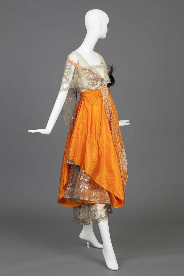 Vintage fashion dress with orange overlay and lace details displayed on a mannequin showcasing centuries of fashion.