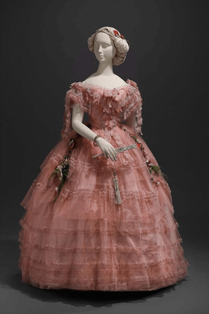 Victorian-era pink lace gown with floral accents on mannequin showcasing centuries of fashion history.