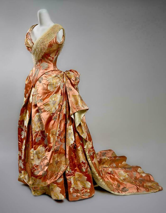 Victorian era orange and gold floral silk dress with a long train, showcasing centuries of fashion history.