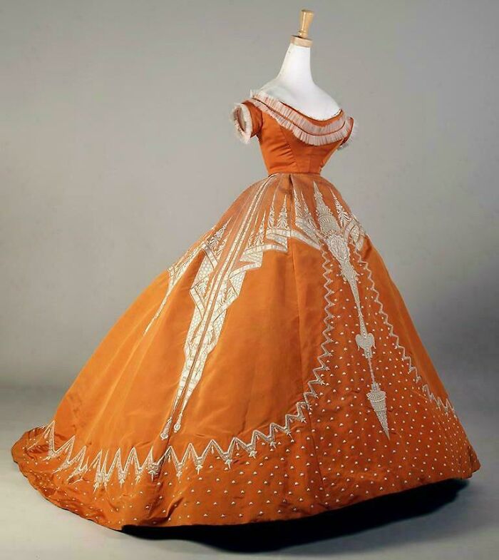 Vintage orange ball gown with intricate embroidery displayed on a mannequin showcasing centuries of fashion history.