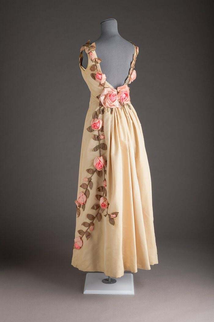 Vintage dress with pink floral appliques displayed on a mannequin, showcasing centuries of fashion evolution.