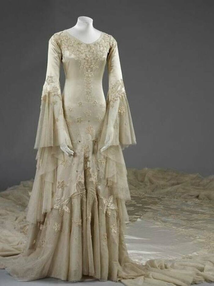 Vintage beige embroidered gown with long layered sleeves displayed, showcasing centuries of fashion evolution in detail.