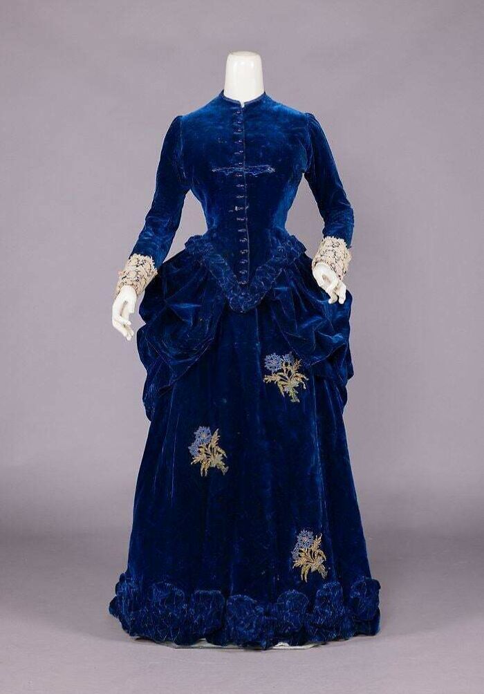 Victorian blue velvet dress with floral embroidery and lace cuffs, showcasing centuries of fashion history on display.