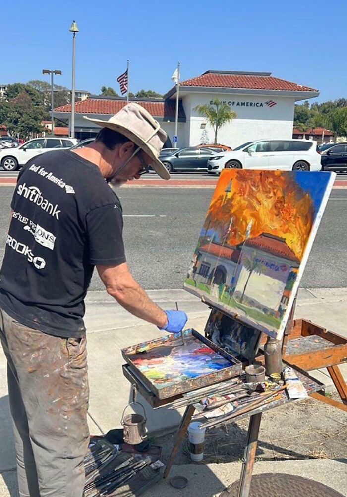 Man painting a blursed image of a building on fire that matches the real Bank of America in the background.