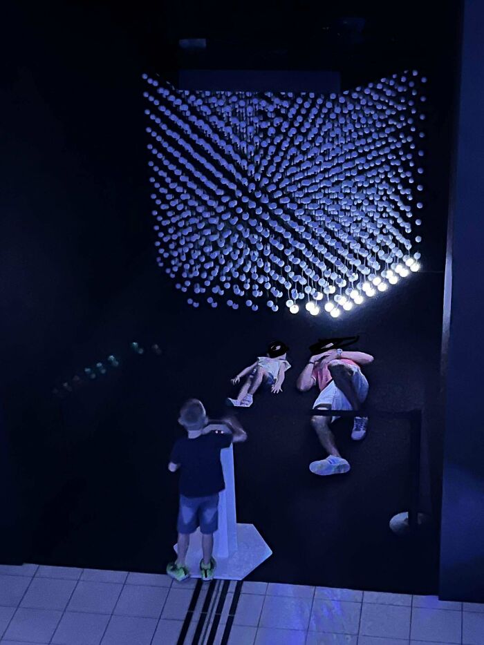 Children and adult tourists interacting with an illuminated art installation in a dark room, showing unusual tourist behavior.