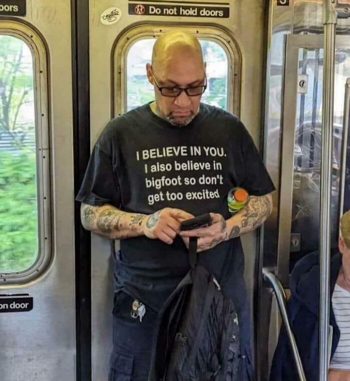 Man on subway wearing a shirt with a humorous message about belief, captured in a blursed image with mind-bending visual elements.