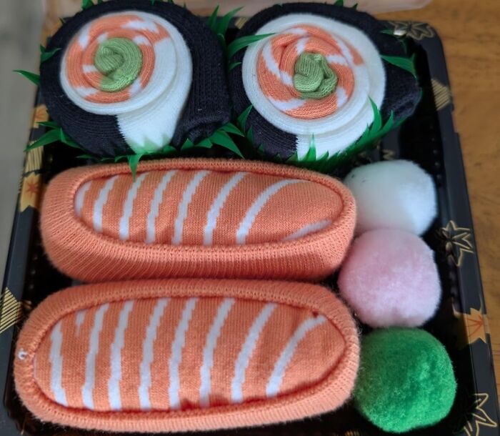 Food-shaped objects resembling sushi rolls and nigiri with colorful pom-poms arranged in a decorative tray.