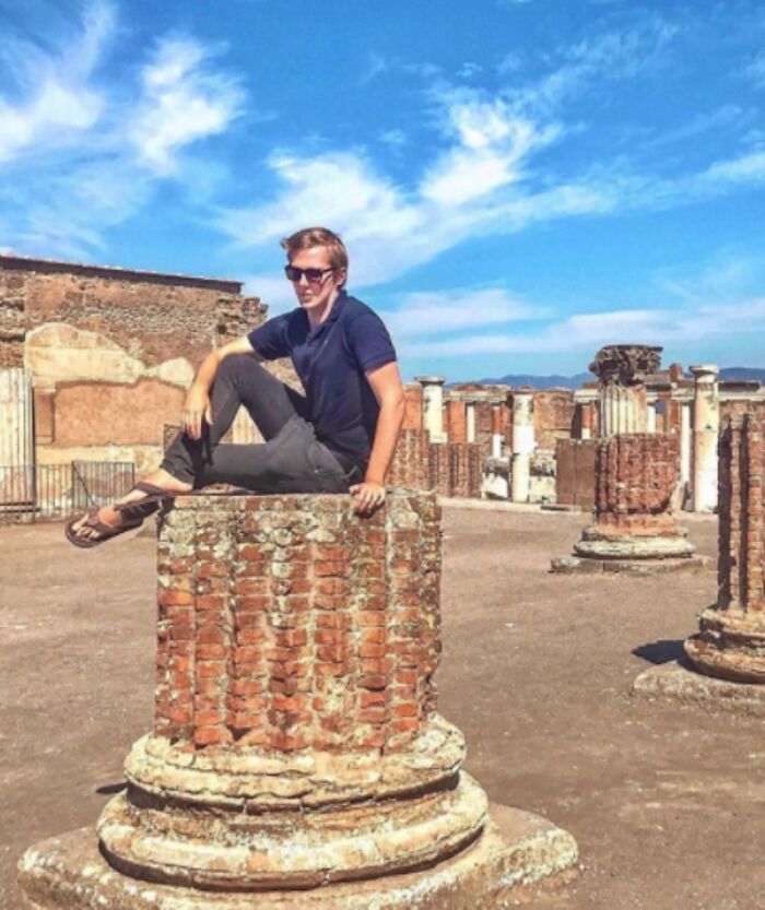 Tourist sitting on a historic ruin column at an ancient site, exhibiting entitled and rude tourist behavior.