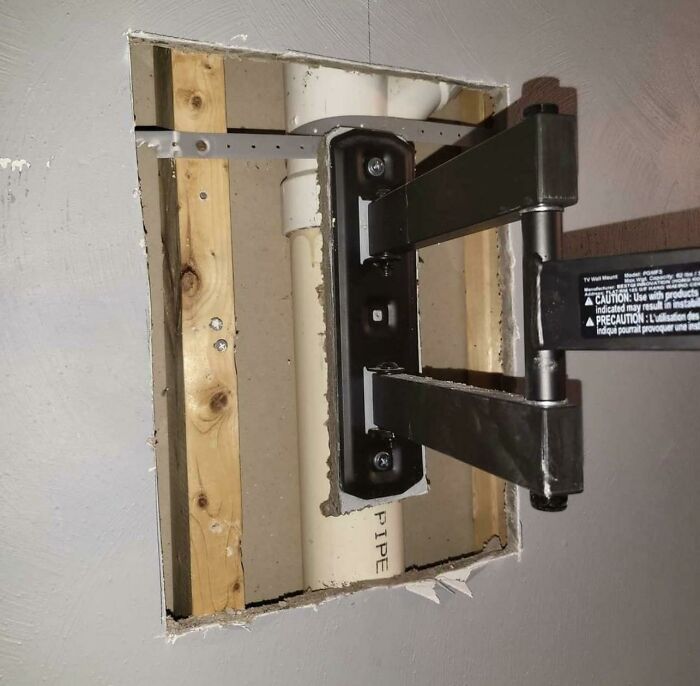 Exposed wall pipe blocked by a TV mount bracket in an infuriating landlord special causing renter frustration.