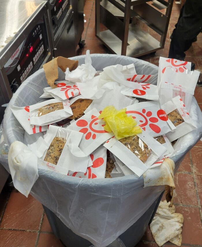 Trash bin overflowing with Chick-fil-A cookie packets and waste, reflecting current life in the US through American eyes.