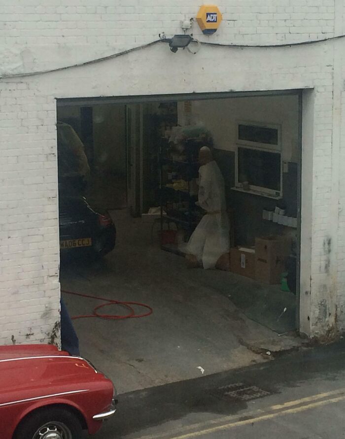 Mannequin in white coveralls in a dimly lit garage creating a creepy scene people came across and shared online.