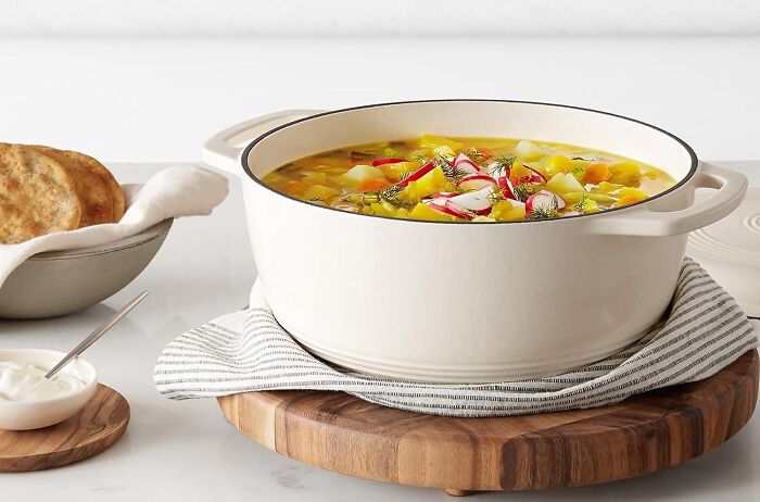 White Dutch oven on wooden board with vegetable soup, highlighting Mother's Day splurges kitchenware gift idea.