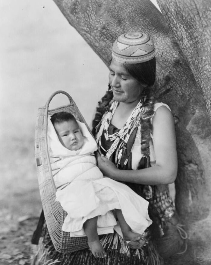 Native American mother holding her baby in a traditional woven cradleboard, showcasing life in the 1900s.