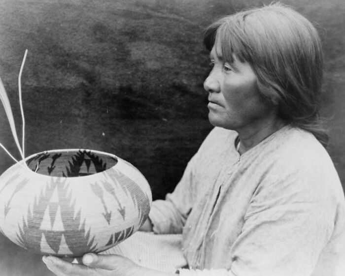 Native American woman in the 1900s holding a decorated pottery bowl, showcasing traditional crafts and culture.