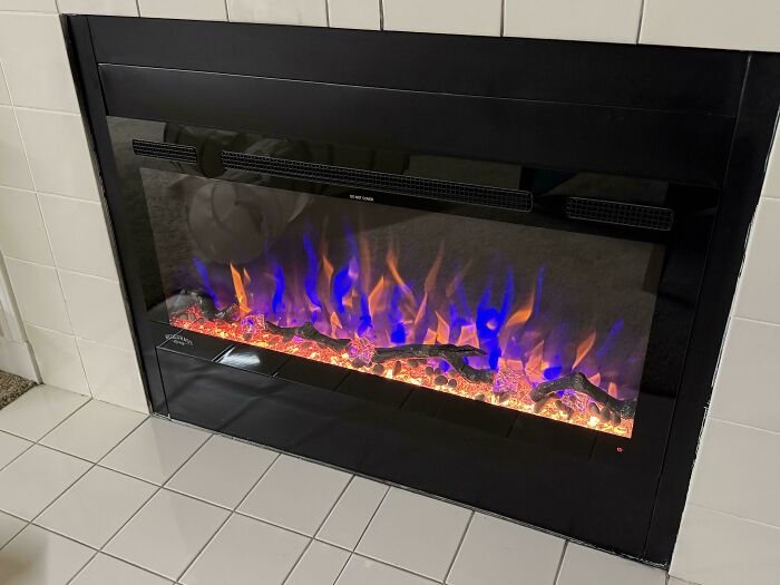 Electric fireplace with blue and orange flames installed in tiled wall, a typical landlord special causing renter frustration.