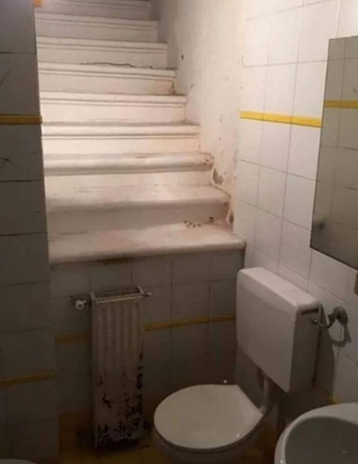 Small bathroom with a toilet and an unusual set of stairs leading directly into the wall, weird pics or it didn’t happen moment.