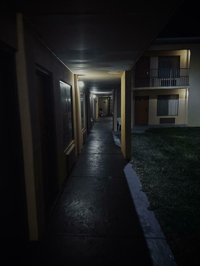 Dimly lit apartment hallway at night with a shadowy figure in the distance, evoking a creepy atmosphere.