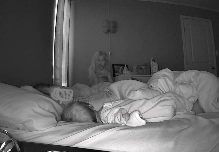 Night vision bedroom scene with people sleeping and a creepy doll figure in the background, creepy encounter shared online.