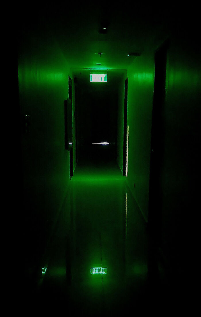 Dark narrow hallway illuminated by glowing green exit signs, creating a creepy and eerie atmosphere.