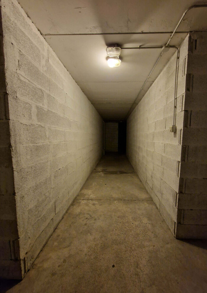 Dimly lit narrow concrete corridor with eerie dark end, evoking creepy feelings often shared by people online.