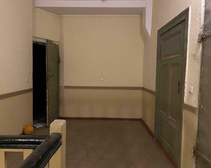 Dimly lit hallway with open dark doorway and old green doors, evoking creepy atmosphere people had to share with others.