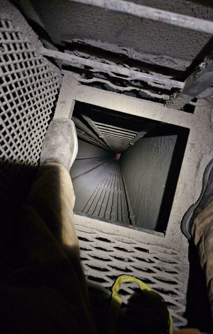 Looking down a dark, narrow shaft with a rusty metal ladder and feet visible, capturing a creepy eerie atmosphere.