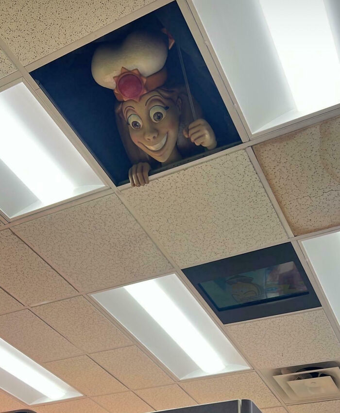 Creepy cartoon character peeking from ceiling tiles in an office, a strange and unsettling sight shared by people online.