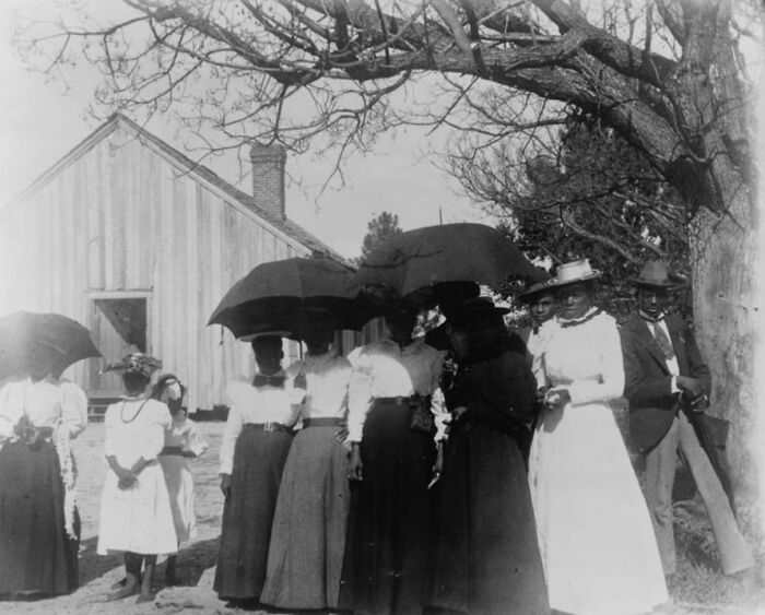 Group of African American women and men from 1900 Paris Exposition standing outdoors with umbrellas and vintage clothing.