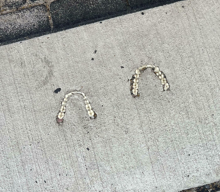 Teeth embedded in a concrete sidewalk forming two creepy arches, a disturbing sight people had to share.