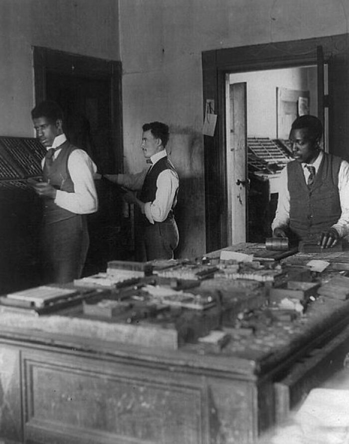 Three African American men in vests working with printing blocks inside a room in early 1900s Paris Exposition.