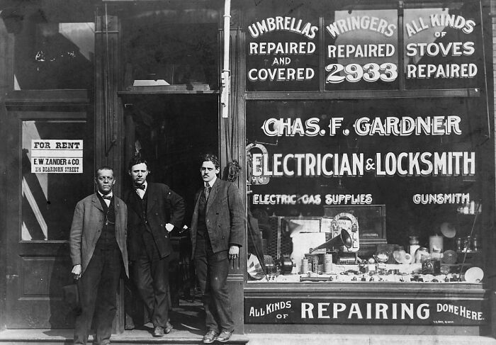 Three African American men standing outside an electrician and locksmith shop in early 1900s urban setting.