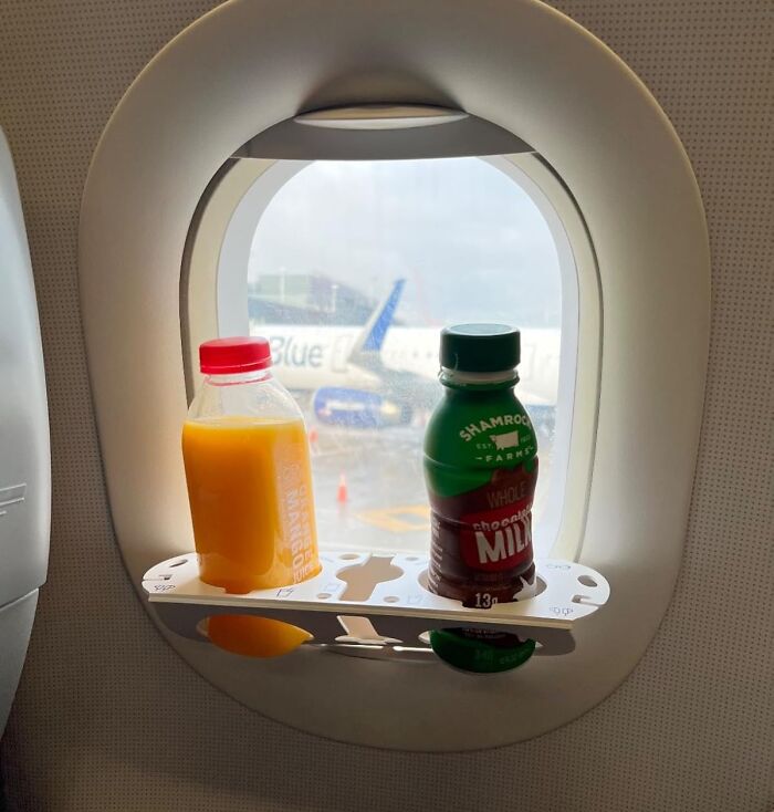 In-flight essentials on a plane tray table with orange juice and chocolate milk by the window for a first-class feeling