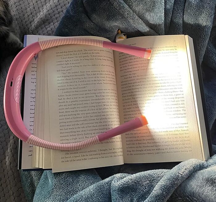 Pink wearable neck reading light resting on an open book, ideal in-flight essential for a first-class feeling on a coach budget.