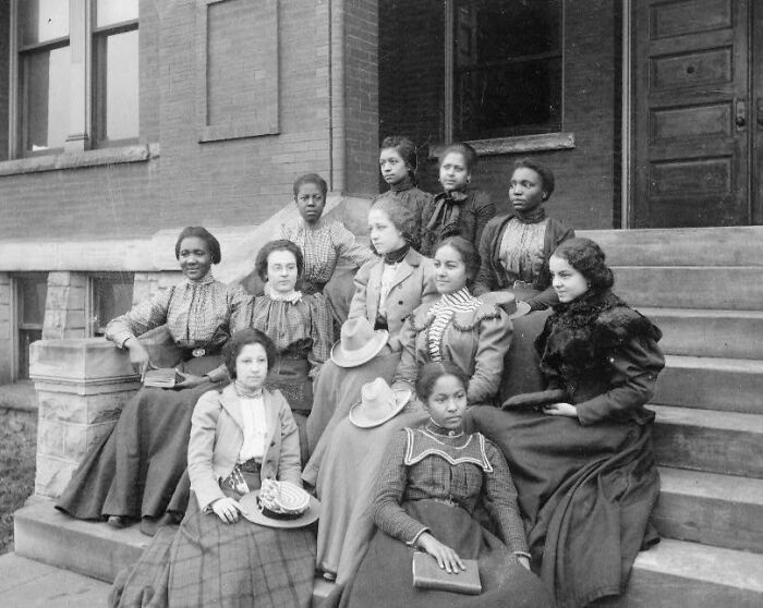 Group of African American women dressed in 1900s attire sitting on steps, capturing African American life history.