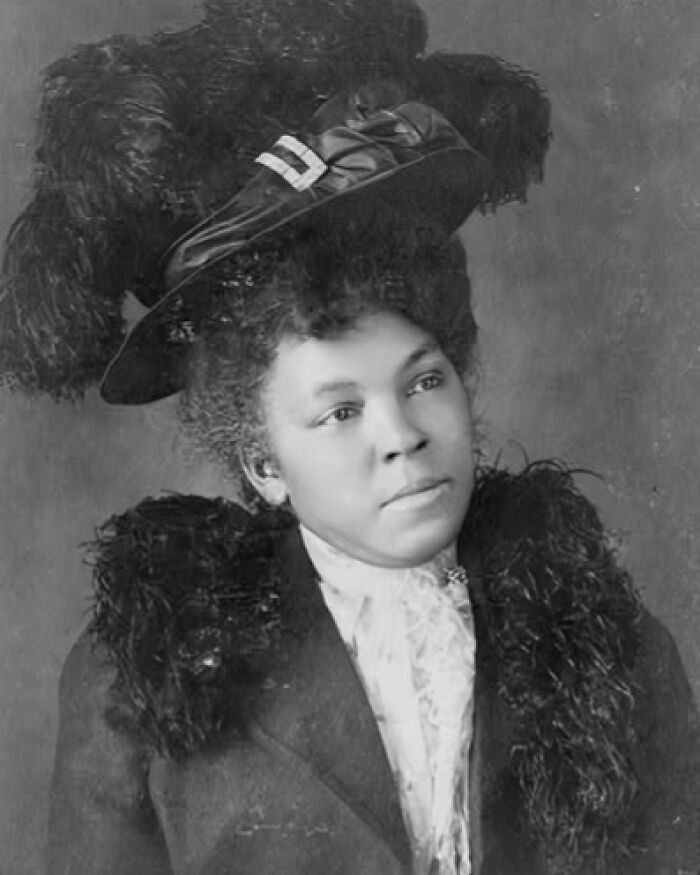 African American woman in early 1900s attire with feathered hat and fur collar, capturing African American life.