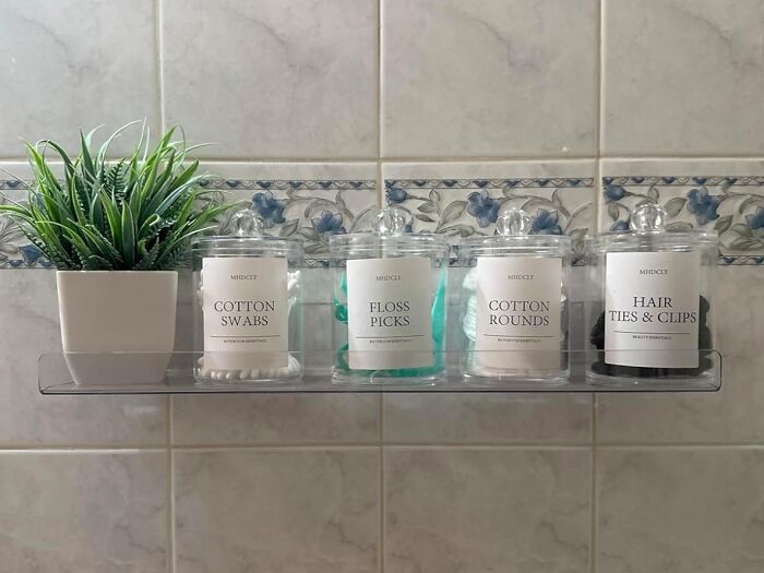 Clear bathroom shelf with affordable home finds including cotton swabs, floss picks, cotton rounds, hair ties, and a small green plant.
