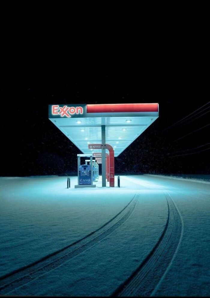 Empty Exxon gas station at night with snow-covered ground and tire tracks, showcasing unsettling yet fascinating empty spaces.