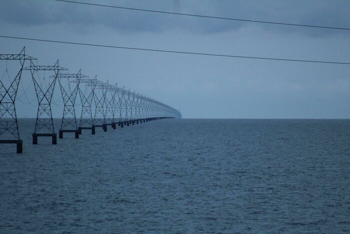 Long row of power lines stretching over empty water space under a gray, unsettling yet fascinating sky.
