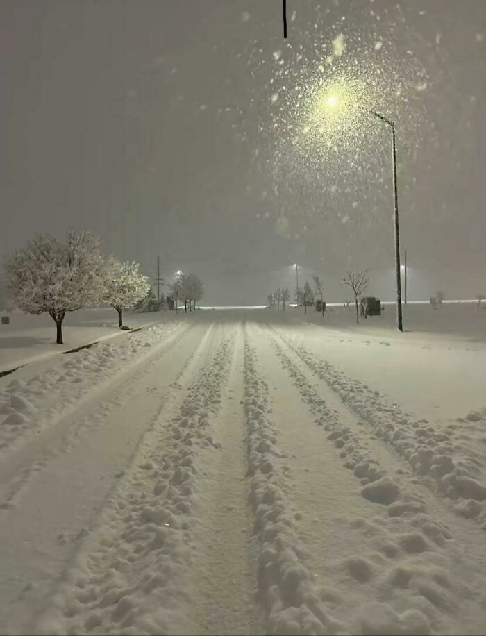 Empty snow-covered street at night with streetlights glowing, creating an unsettling yet fascinating empty space atmosphere.